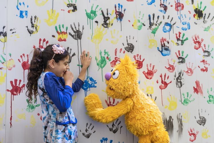 Jad and a young girl pose against a mural of colorful handprints