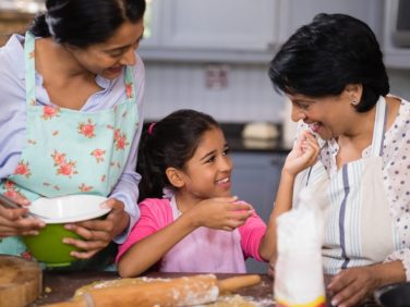 A young girl, her mom, and grandmother rolling dough and baking together.