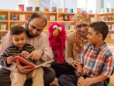 A husband and wife reading to Elmo and their two kids.
