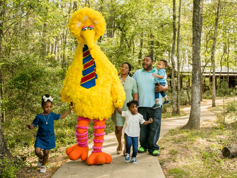 Big Bird holds the hands of two children while walking with their family.