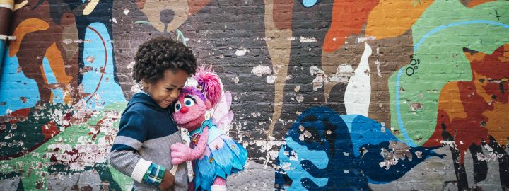 Abby hugs a young boy in front of a brick wall with a colorful, abstract mural.
