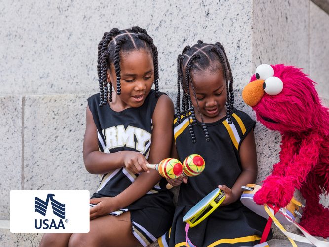 Elmo playing with two cheerleaders and maracas.