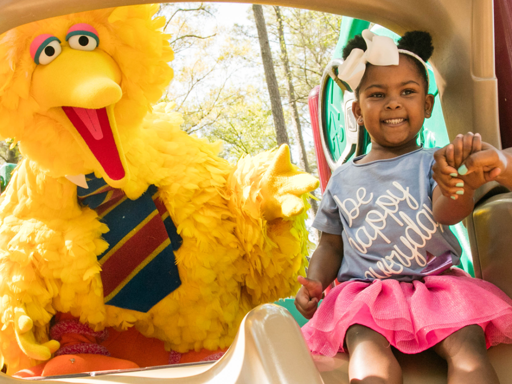 A child going down a slide with big bird and mother.