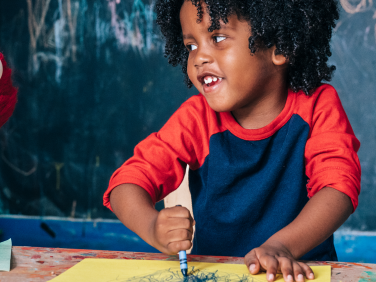 A young child smiles while coloring with Elmo.