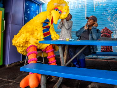 A child whispering to Big Bird at a picnic table.