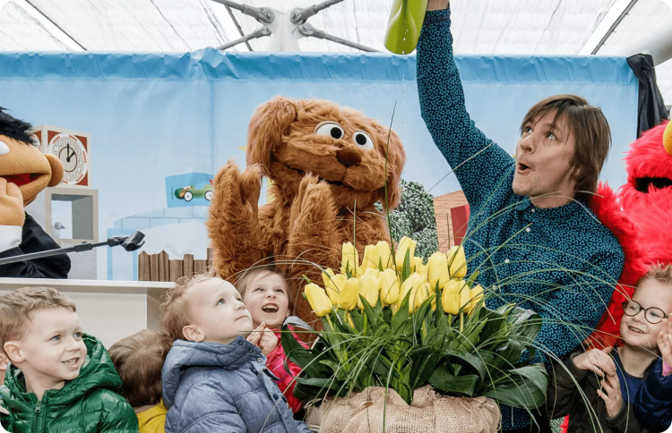 Sesame Street Muppets and a crowd of children watering tulips.