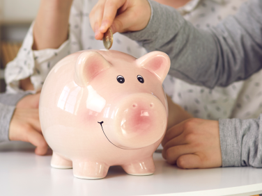 A child adds money into a classic pink piggy bank.