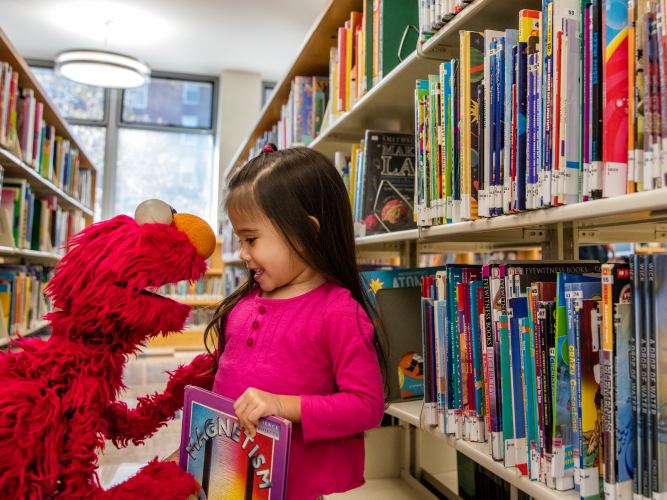 Elmo in a library with a little girl.
