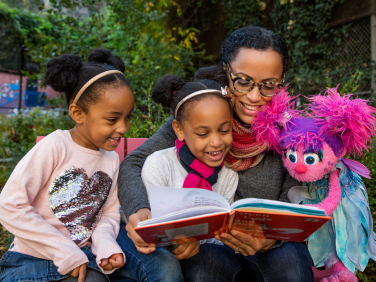 A mother reads to her two daughters with Abby Cadabby.