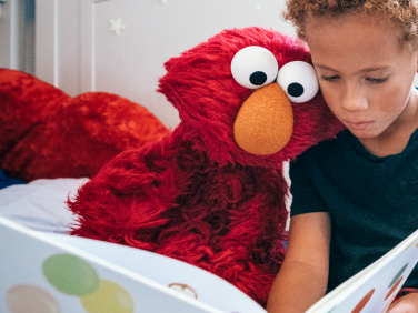 Elmo and a young boy read a book together.