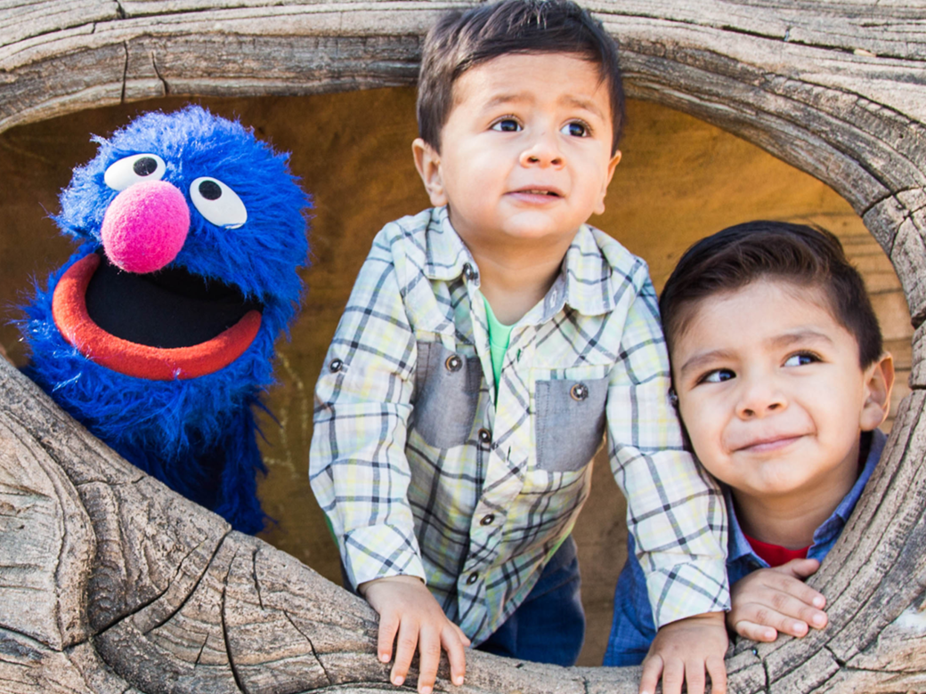 Two kids with Grover peaking out of a tree.