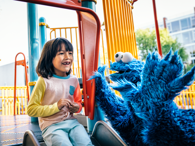 Little girl and Cookie Monster playing on a slide