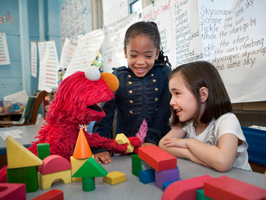 Elmo playing blocks with two girls.
