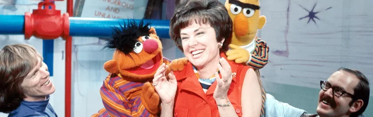 Joan Ganz laughing as Bert and Ernie sit on her shoulders.